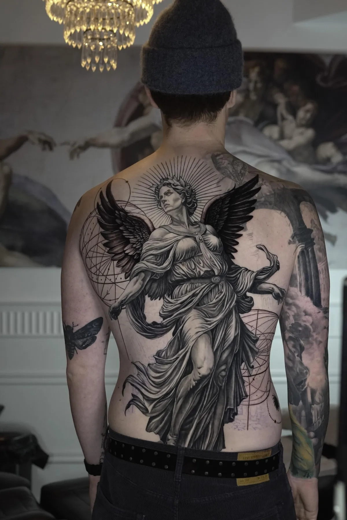 Stor black and grey-tatuering av en bevingad ängelstaty över hela ryggen