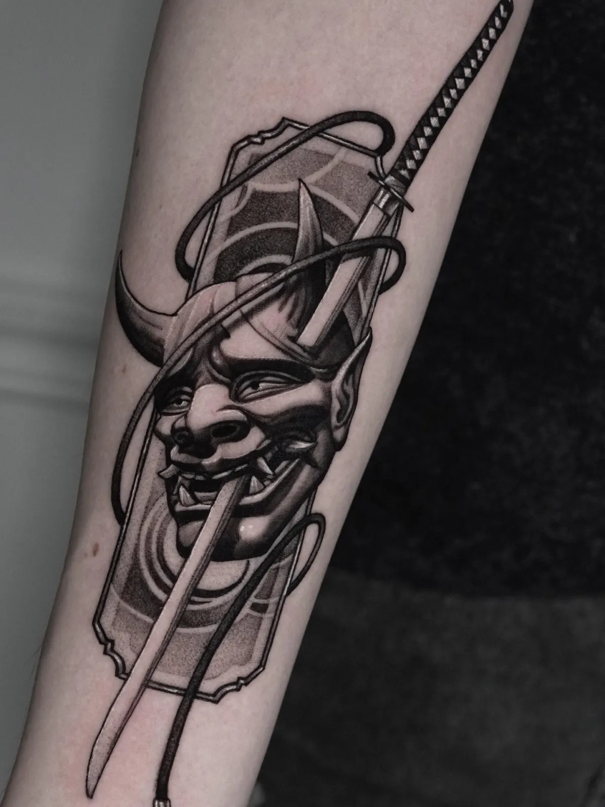 Hannya-mask med katana tatuerad i black and grey på underarmen